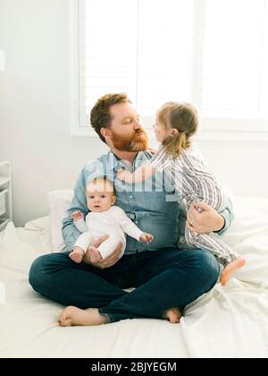 Father sitting on bed with children (2-3 months, 2-3) Stock Photo