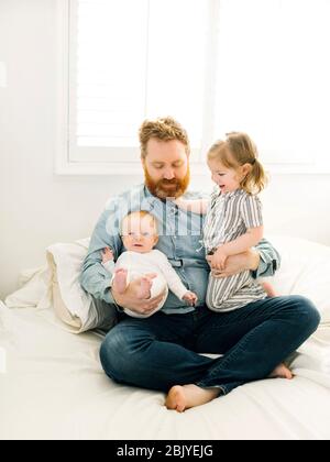 Father sitting on bed with children (2-3 months, 2-3) Stock Photo