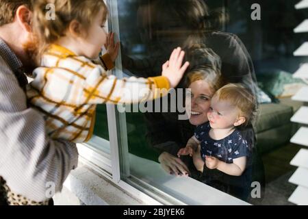 Family with daughters (2-3) visiting through window