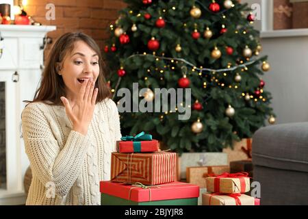 Surprised young woman with Christmas gifts at home Stock Photo