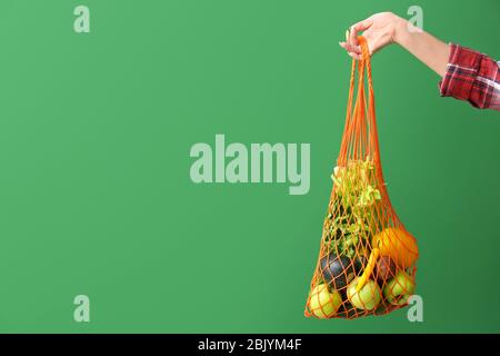 Female hand holding mesh eco bag with products on color background Stock Photo