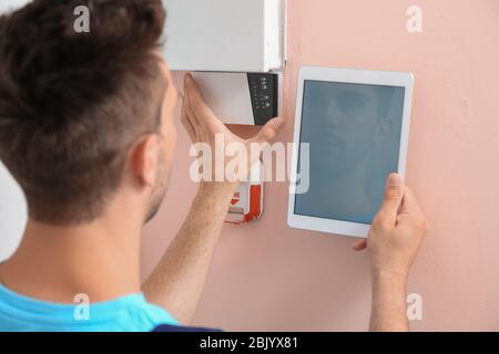 Electrician with tablet computer checking alarm system indoors Stock Photo