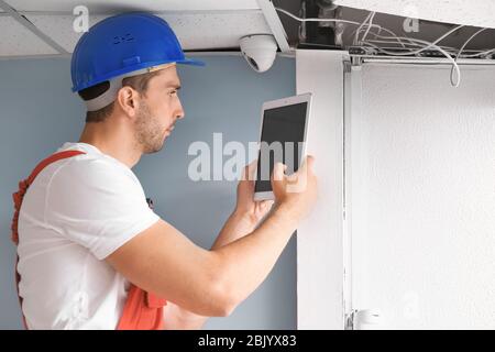 Electrician with tablet computer installing alarm system indoors Stock Photo