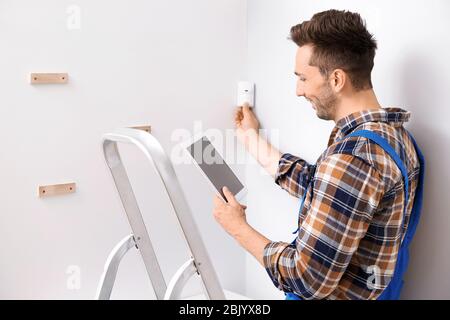 Electrician with tablet computer installing alarm system indoors Stock Photo