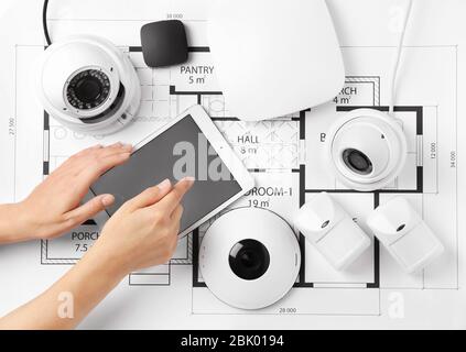 Female hands with tablet computer and different equipment of security system on home plan Stock Photo