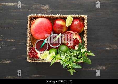 Wicker box with fruits and pomegranate juice on dark wooden background Stock Photo