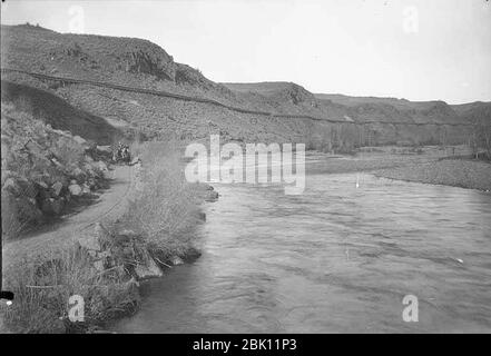 Horse-drawn wagon on road beside Naches River with irrigation flume along hills near North Yakima April 17 1896 (WAITE 39). Stock Photo