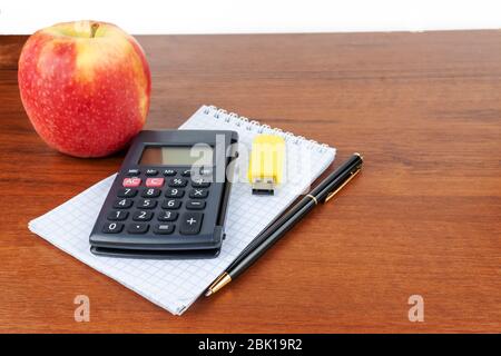 An apple, a calculator, pen, flash drive, notebook, lie on the table. Stock Photo