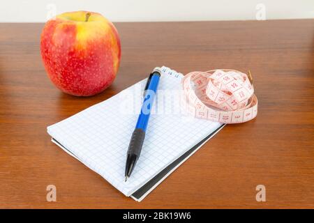 An apple, a notebook, a measuring tape, a pencil lie on a table. Stock Photo