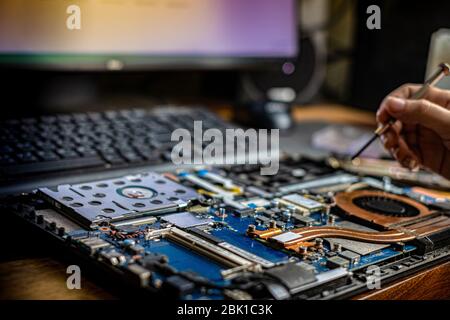 Hand technician repairing broken laptop notebook computer with a screwdriver Stock Photo