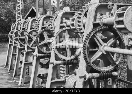 Gear wheels, toothed belts, chains, shafts and racks at a weir on the river Aller, Germany, black and white Stock Photo