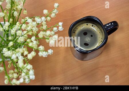 High angle of spring flowers (lily of the valley) and coffee cup on wooden table Stock Photo