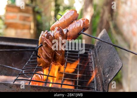 Sausage stabbed on an iron fork and toasted over an fire. Old rusty metal grill. Burning logs in a barbecue grill. Stock Photo