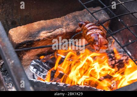 Sausage stabbed on an iron fork and toasted over an fire. Old rusty metal grill. Burning logs in a barbecue grill. Stock Photo