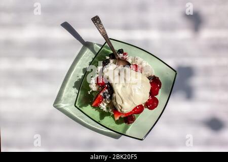 Plate with cottage cheese with sour cream and strawberries with raisins in the style of a flat lay. The glass plate is green. Silver teaspoon inside. Stock Photo