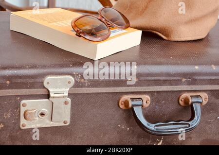Vintage suitcase with sunglasses, book and hat. Ancient brown suitcase for journey. Stock Photo