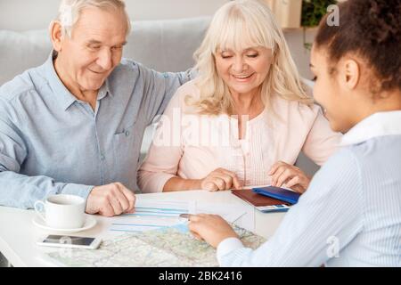 Travel agent at office sitting explaining contract to senior clients joyful Stock Photo