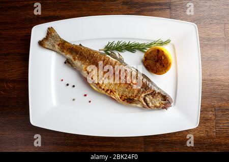Grilled trout with resemary and lemon served on a white plate in a restaurant Stock Photo