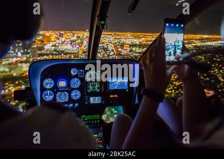 View pilot and client taking mobile phone pictures in helicopter flight over Vegas at night, Las Vegas, Nevada, USA, North America Stock Photo