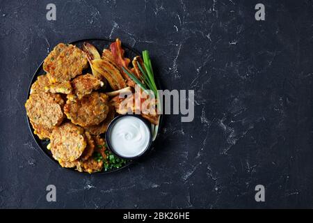 sweet corn cottage cheese pancakes with the caramelized banana, fried bacon, spring onion and sour cream on a black plate on a concrete table, horizon Stock Photo