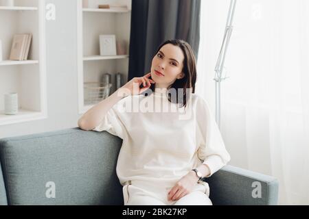 Beautiful elegant woman in white relaxing on sofa. Stock Photo