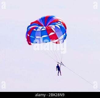 Parachuter descending with a parachute against blue sky Stock Photo