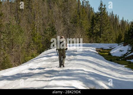 Man with big backpack walks along the snow covered road in spring Stock Photo