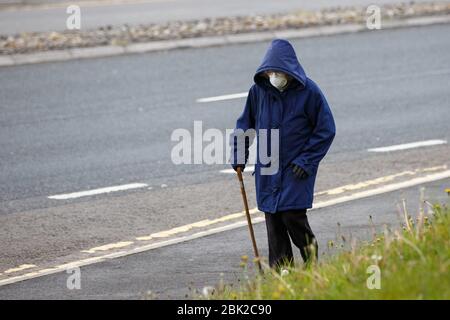 Carmarthen, UK. 1 May, 2020. An elderly woman wearing a face mask to protect her from Coronavirus, and walking with a stick, takes her daily exercise in Carmarthen, west Wales. Credit: Gruffydd Ll. Thomas/Alamy Live News Stock Photo