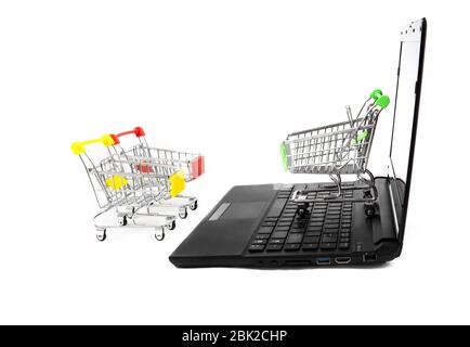 Three empty miniature shopping carts stand close to a black laptop isolated on white. E-commerce concept. Stock Photo