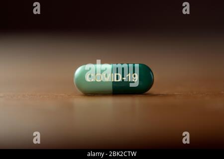 A pill with the text covid-19 printed on it on a wooden table Stock Photo