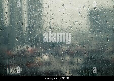 Closeup raindrops water droplets trickling down on wet clear window glass during heavy rain against blurred city view in rainy day monsoon season Stock Photo