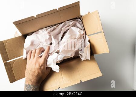 Closeup of man with tattoos packing parcels with crumpled paper isolated on white background. Stock Photo