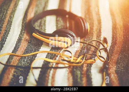 Bright yellow large headphones for listening to music lie on a soft woolen striped blanket, illuminated by warm sunlight. Stock Photo