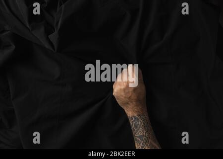 Man hand with tattoos holding wrinkle black fabric texture. Stock Photo