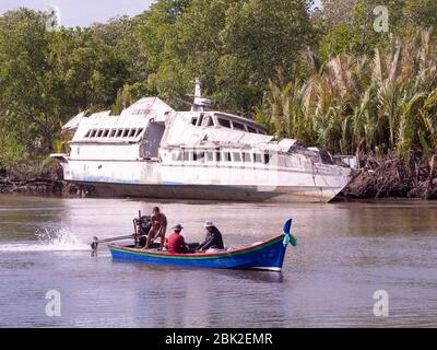 Small long tail passenger vessel on Mak Bang, Satun City, Satun in the south of Thailand. Wreck of passenger ferry on the shore in the background. Stock Photo