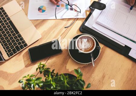 Top view of cup of hot cappuccino art coffee on wooden table with businesspeople working on some documents. Cup of coffee with milk foam art pattern o Stock Photo