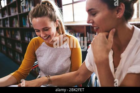 Woman sitting in a wheelchair writing in a notebook with a female teacher sitting by at school. Disabled female student studying with tutor. Stock Photo