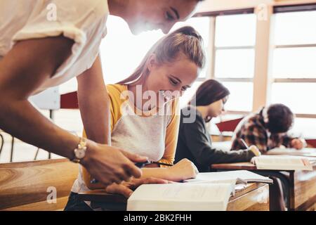 Young woman studying with teacher standing by in classroom. High school teacher helping student in classroom. Stock Photo