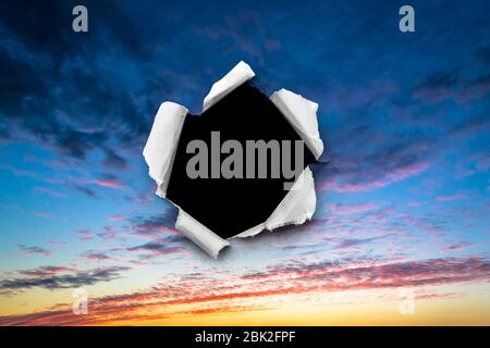 A hole in the sunset sky with torn edges, as on paper, with an isolated black space background in the center. The concept of global climate change on Stock Photo