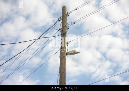 Electric wooden pole with lamp and electricity cables hanging on. Cloudy sky. Stock Photo