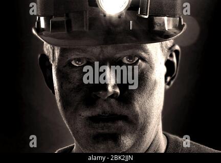 Tired dirty face of coal miner in helmet with light. Detailed portrait of mine worker. Stock Photo