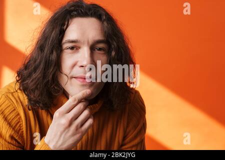 Image closeup of pleased young man posing and looking at camera isolated over orange wall with light Stock Photo