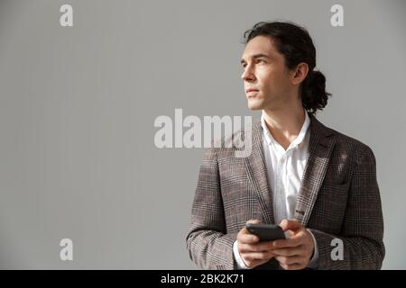 Image of focused handsome man in jacket looking aside and using cellphone isolated over white background Stock Photo