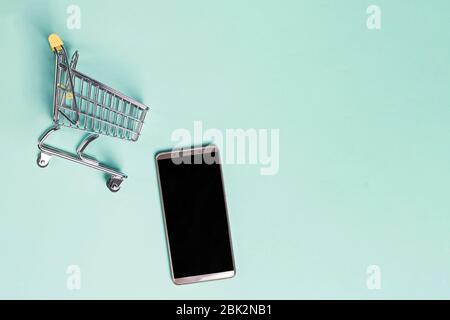 Smartphone and small shopping trolley on blue background Stock Photo