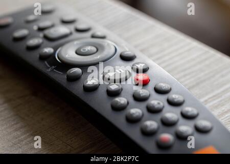 A portrait of a television infrared remote control lying on a wooden table. The focus is on the play and pause button. It can also be used to control Stock Photo