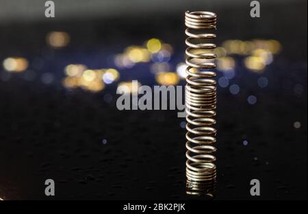 Metal spring on a black background. Precision mechanics. Small items. Part of the pen. Shiny background. Mold and drops of water. Gold and silver. Stock Photo