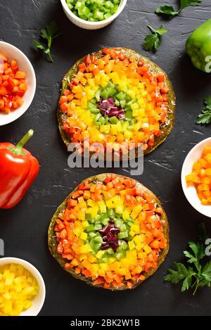Rainbow veggie bell peppers pizza crust on black stone background. Vegetarian vegan or healthy food concept. Gluten free diet dish. Top view, flat lay Stock Photo