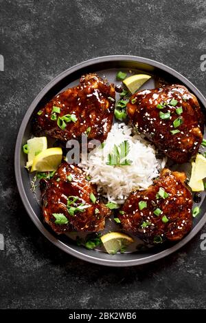 Sweet and spicy honey grilled chicken thighs with rice over dark stone table. Tasty food in asian style. Top view, flat lay Stock Photo