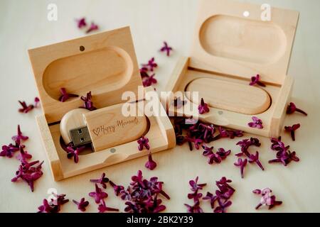 Wooden brown usb flash drives with boxes with the text Happy Moments with lilac petals on a white background, data storage, beautiful feedback to clie Stock Photo