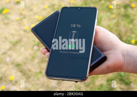 Smartphone charging without cable from induction power bank in the woman hand. Modern technology concept. Selective focus. Stock Photo